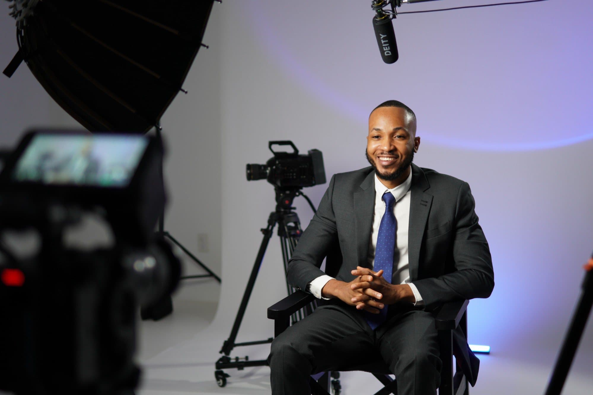 A smiling man in a suit seated for an interview on a film studio set